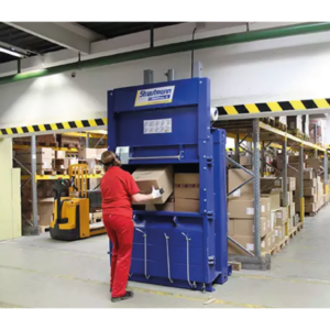 A staff member in a warehouse packs cardboard boxes into a BP18 baler machine.