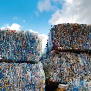 Large stacks of plastic bottles baled into cubes stood outside with the sky above.