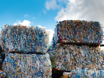 Large stacks of plastic bottles baled into cubes stood outside with the sky above.