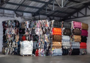 Large stacked bales of recycled fabrics in a warehouse.