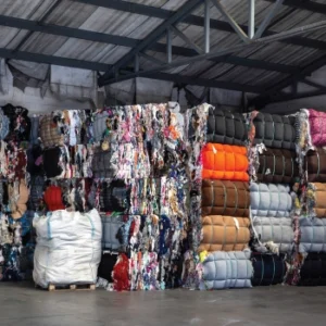 Large stacked bales of recycled fabrics in a warehouse.