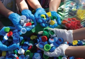 Hands in latex gloves hold loose bottle caps in a recycling plant.