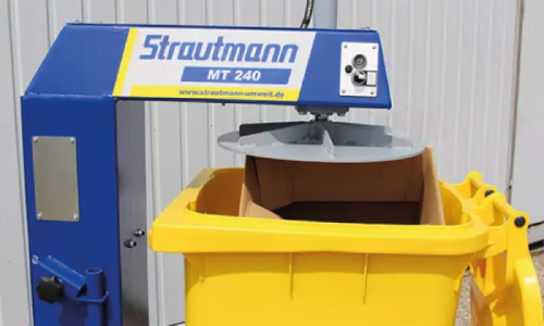 A wheelie bin plate compactor over a wheelie bin filled with cardboard.